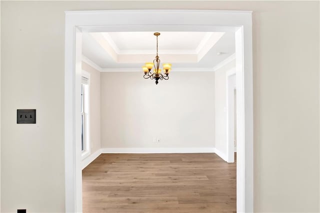 unfurnished dining area featuring a tray ceiling, crown molding, wood-type flooring, and a notable chandelier