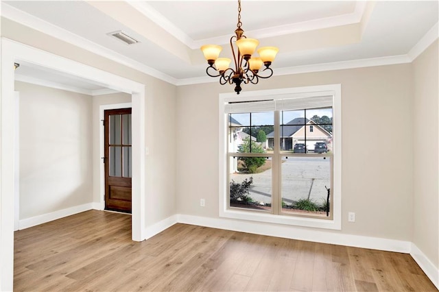 unfurnished dining area with a raised ceiling, light hardwood / wood-style flooring, ornamental molding, and an inviting chandelier