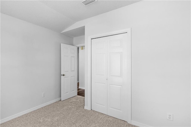 unfurnished bedroom featuring lofted ceiling, carpet floors, visible vents, baseboards, and a closet