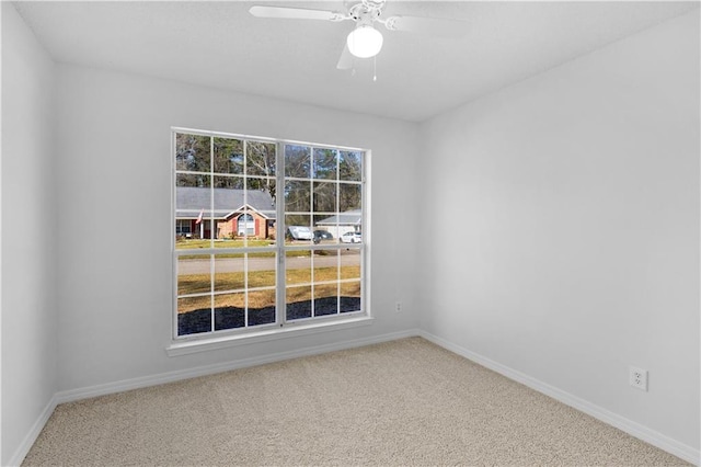 carpeted spare room featuring baseboards and a ceiling fan