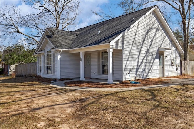 view of side of home featuring covered porch, a shingled roof, and fence