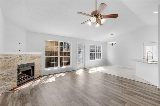 unfurnished living room with vaulted ceiling, a stone fireplace, a textured ceiling, and light wood-type flooring