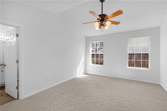 carpeted empty room featuring ceiling fan, baseboards, vaulted ceiling, and a textured ceiling