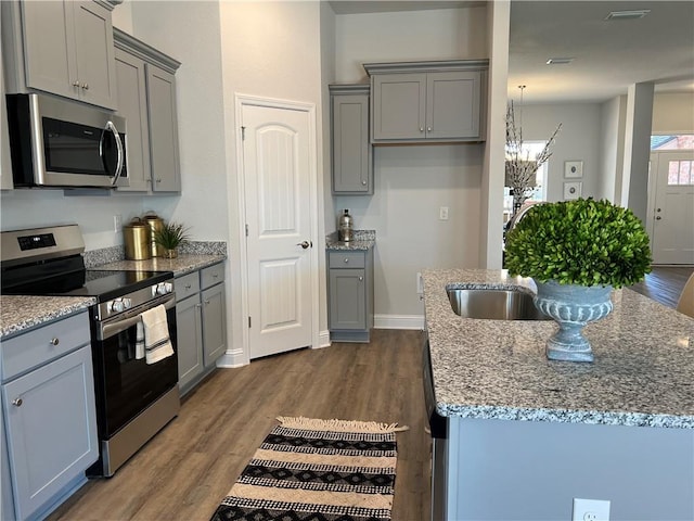 kitchen featuring sink, gray cabinetry, dark wood-type flooring, stainless steel appliances, and an island with sink