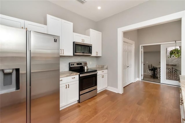 kitchen with stainless steel appliances, white cabinetry, decorative backsplash, and light wood finished floors