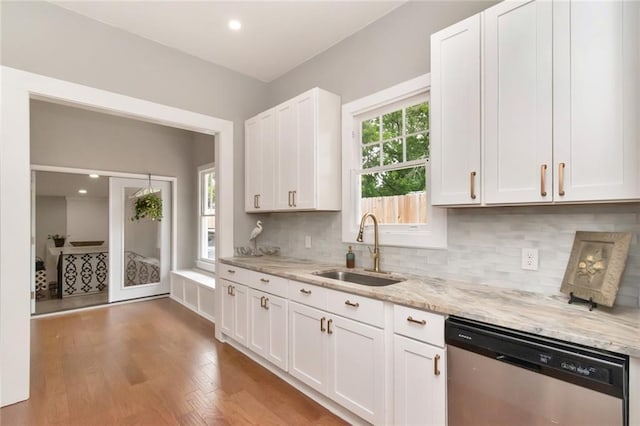 kitchen with wood finished floors, light stone countertops, a sink, white cabinets, and stainless steel dishwasher