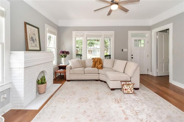 living area featuring a fireplace, ceiling fan, and wood finished floors