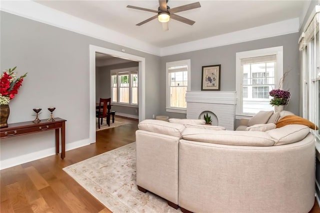 living room featuring a brick fireplace, wood finished floors, baseboards, and ceiling fan