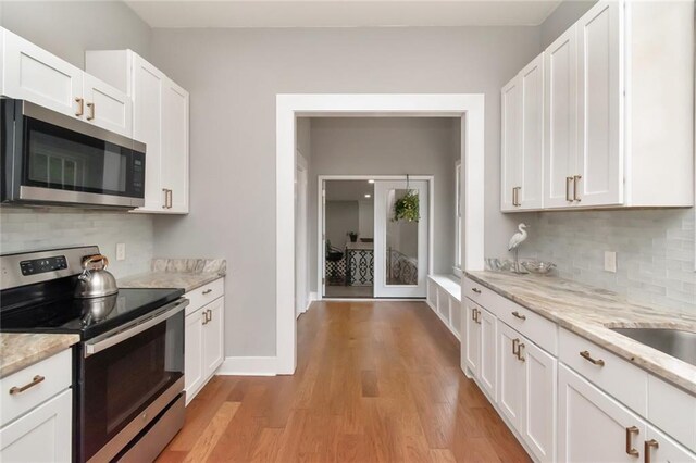 kitchen with white cabinets, backsplash, light wood-type flooring, and appliances with stainless steel finishes