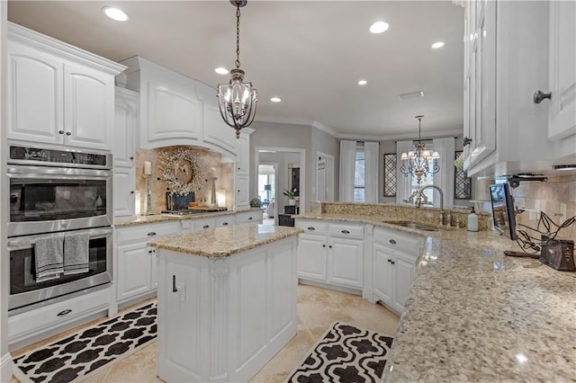 kitchen with hanging light fixtures, white cabinetry, sink, and light stone counters