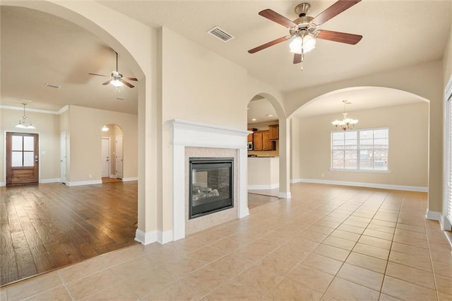 unfurnished living room featuring ceiling fan with notable chandelier, a fireplace, and light tile patterned floors