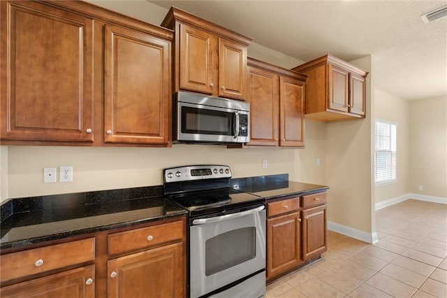 kitchen featuring dark stone countertops, light tile patterned floors, and appliances with stainless steel finishes