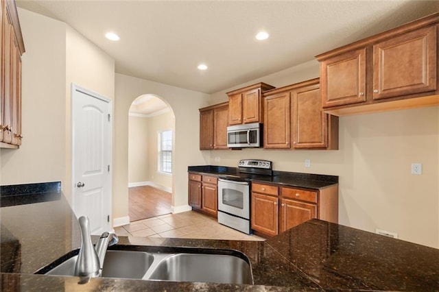 kitchen featuring sink, stainless steel appliances, dark stone countertops, and light tile patterned flooring