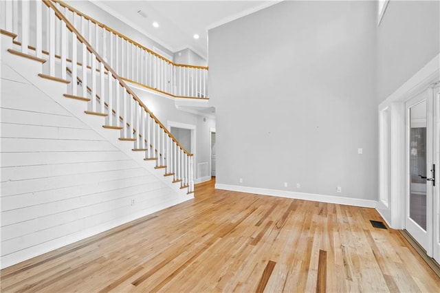 foyer entrance featuring wood walls, crown molding, light hardwood / wood-style floors, and a high ceiling