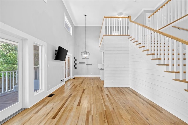 interior space with a towering ceiling, crown molding, wooden walls, hardwood / wood-style floors, and a chandelier