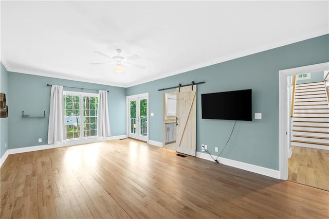 unfurnished living room featuring wood-type flooring, ornamental molding, a barn door, and ceiling fan