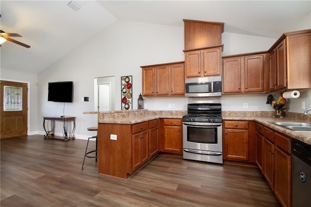 kitchen with a peninsula, appliances with stainless steel finishes, brown cabinetry, and a sink