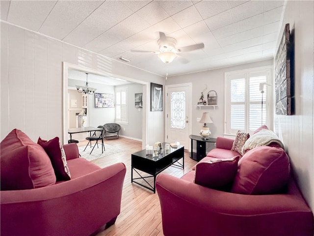 living room with ceiling fan with notable chandelier, light wood-style floors, and baseboards