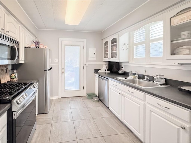 kitchen with a sink, dark countertops, appliances with stainless steel finishes, white cabinets, and glass insert cabinets