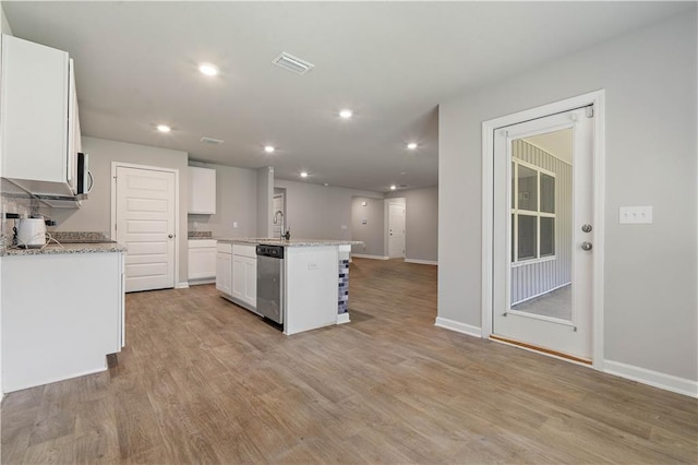 kitchen with light stone countertops, a kitchen island with sink, white cabinets, and stainless steel dishwasher