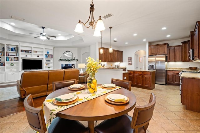 tiled dining room featuring a raised ceiling, ceiling fan with notable chandelier, and built in features