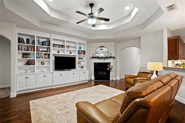 living room featuring dark hardwood / wood-style floors, a raised ceiling, and ceiling fan