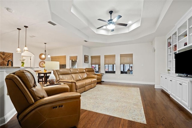 living room featuring dark hardwood / wood-style flooring, a tray ceiling, and ceiling fan