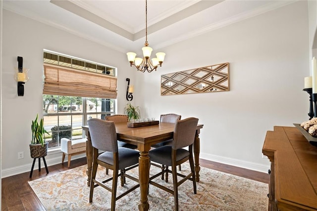 dining space with ornamental molding, dark wood-type flooring, an inviting chandelier, and a tray ceiling