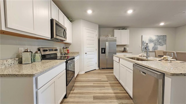 kitchen featuring appliances with stainless steel finishes, sink, white cabinets, a center island with sink, and light wood-type flooring