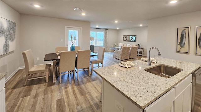 kitchen with sink, white cabinets, light stone counters, a center island with sink, and light wood-type flooring