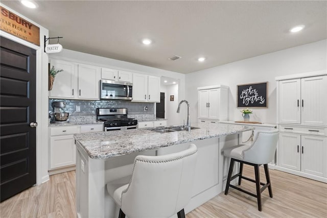 2526 Windmere Dr E, Semmes, AL 36575 - kitchen featuring a breakfast bar area, light wood-type flooring, white cabinets, a sink, and stainless steel appliances