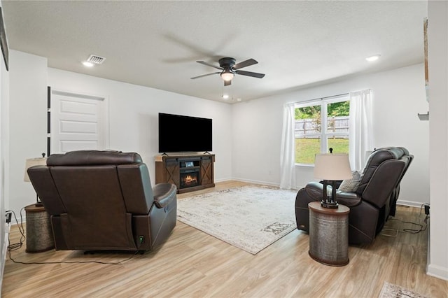 2526 Windmere Dr E, Semmes, AL 36575 - living room with a warm lit fireplace, ceiling fan, light wood-style floors, baseboards, and visible vents