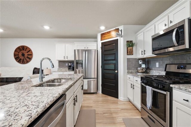 2526 Windmere Dr E, Semmes, AL 36575 - kitchen featuring appliances with stainless steel finishes, a sink, white cabinetry, decorative backsplash, and light wood-type flooring