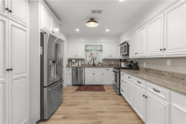 4689 Oak Ridge Rd, Mobile, AL 36609 - kitchen featuring appliances with stainless steel finishes, white cabinets, light wood finished floors, light stone countertops, and ornamental molding