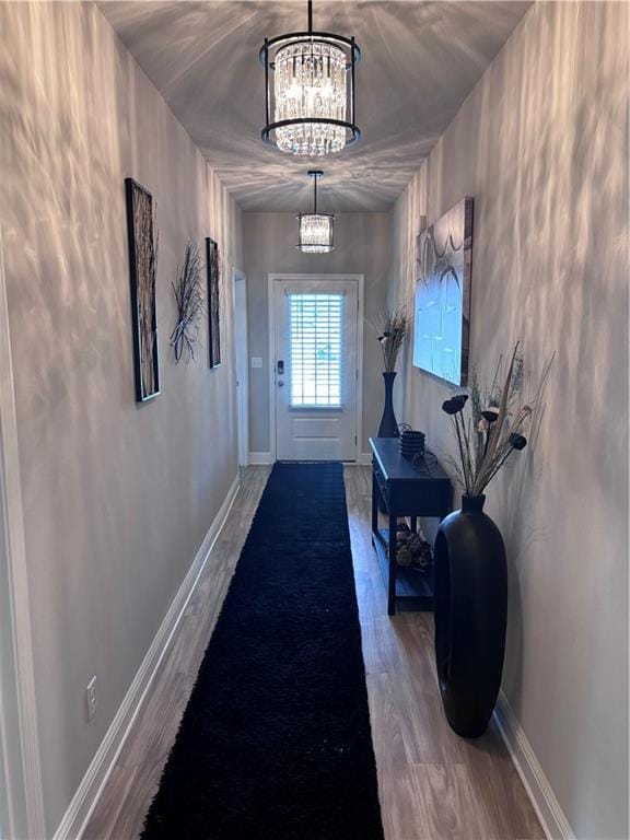 doorway to outside featuring a chandelier, wood finished floors, and baseboards