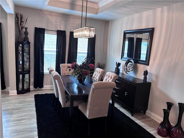 dining area featuring crown molding, light wood finished floors, baseboards, and a raised ceiling