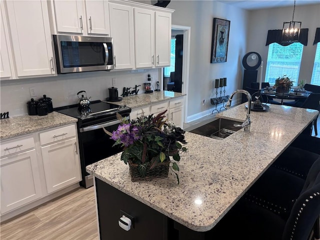 kitchen with white cabinets, a sink, stainless steel microwave, light wood-style floors, and black range with electric stovetop