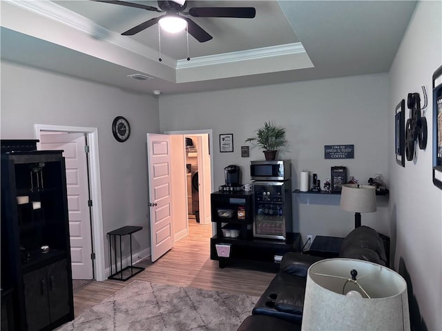 living room with beverage cooler, a raised ceiling, wood finished floors, a ceiling fan, and ornamental molding