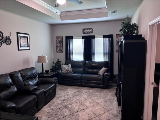 living area with visible vents, light wood-style floors, a ceiling fan, ornamental molding, and a raised ceiling