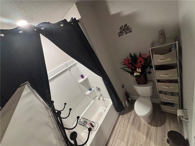 full bath featuring wood finished floors, a tub, a textured ceiling, and toilet