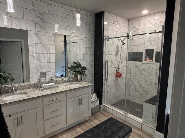 bathroom featuring double vanity, wood finished floors, a stall shower, and a sink