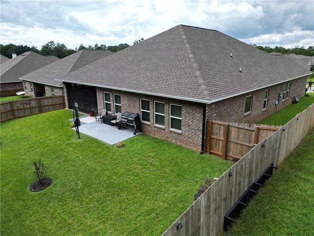 rear view of property featuring a patio area, a shingled roof, a fenced backyard, a yard, and brick siding