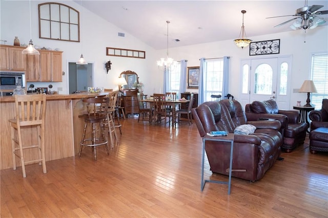 living room featuring ceiling fan with notable chandelier, light hardwood / wood-style flooring, and high vaulted ceiling