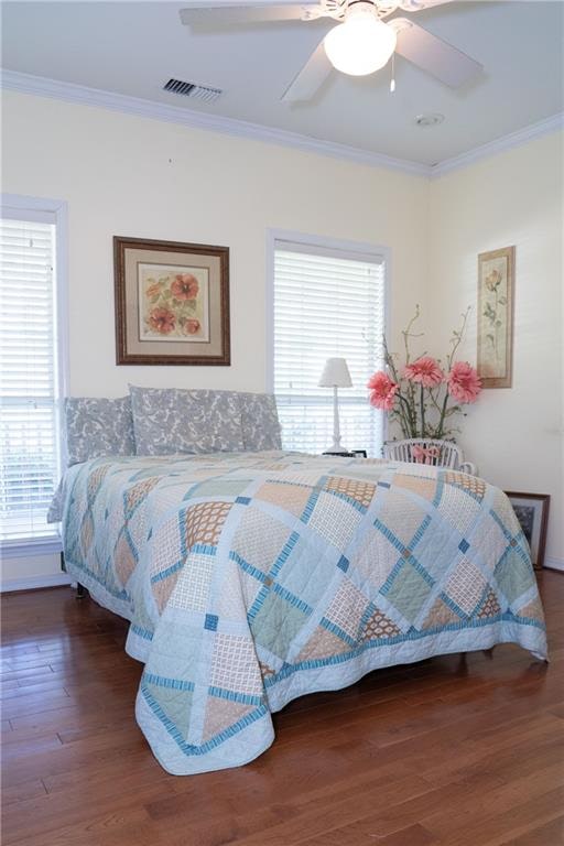 bedroom featuring dark hardwood / wood-style floors, ornamental molding, ceiling fan, and multiple windows