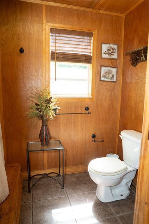 bathroom featuring tile floors, wooden walls, and toilet