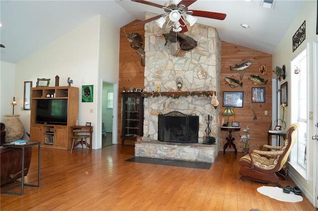 living room featuring ceiling fan, a fireplace, high vaulted ceiling, wood walls, and hardwood / wood-style flooring