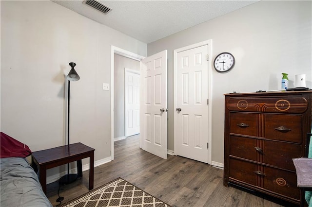 bedroom featuring visible vents, a textured ceiling, baseboards, and wood finished floors