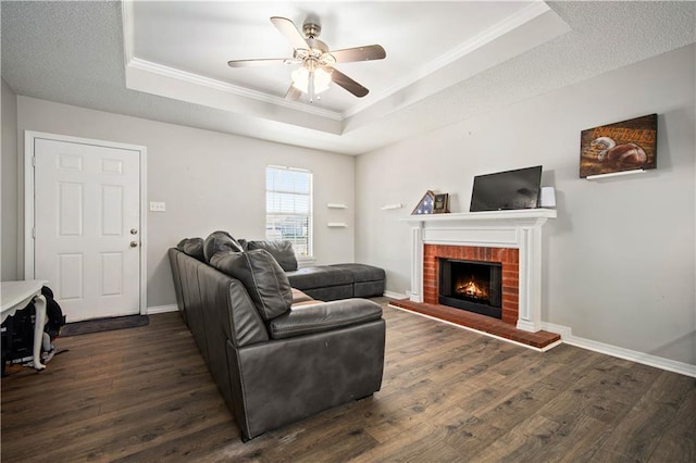 living room with crown molding, a tray ceiling, dark wood finished floors, and baseboards