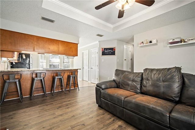 living area with dark wood-style flooring, a raised ceiling, visible vents, and crown molding