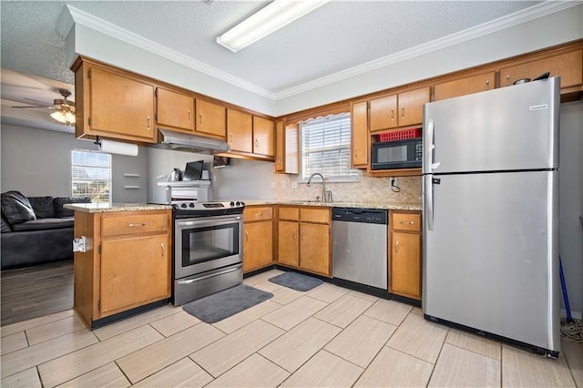 kitchen featuring appliances with stainless steel finishes, brown cabinetry, a sink, a peninsula, and under cabinet range hood